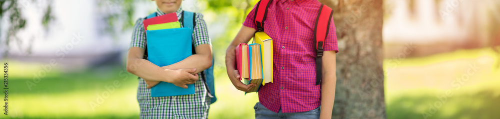 背着帆布背包的孩子站在学校附近的公园里。背着书和背包的学生在户外