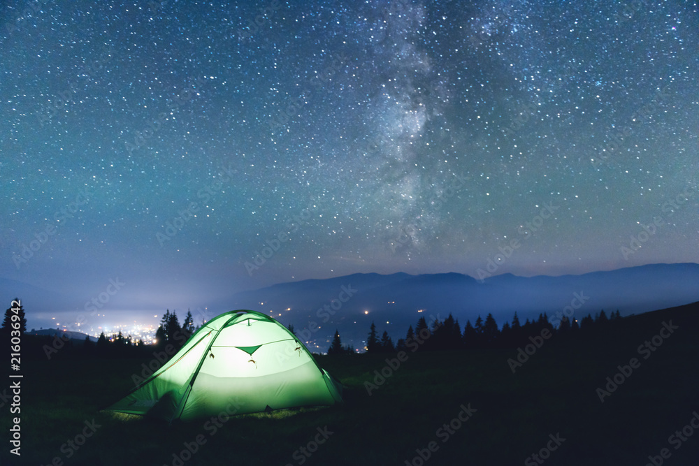 在难以置信的星空背景下，绿色帐篷由手电筒从内部照亮。