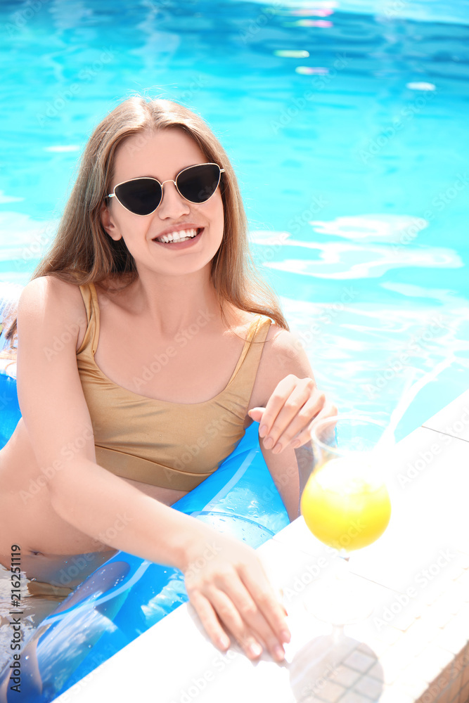 年轻女子在泳池游泳时伸手拿鸡尾酒