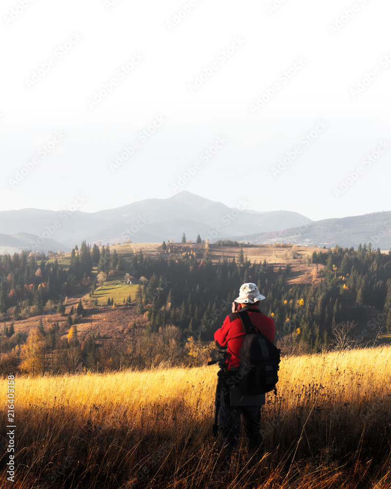 Photographer taking photo of autumn landscape with foggy peaks and orange trees. Ukrainian Carpathia
