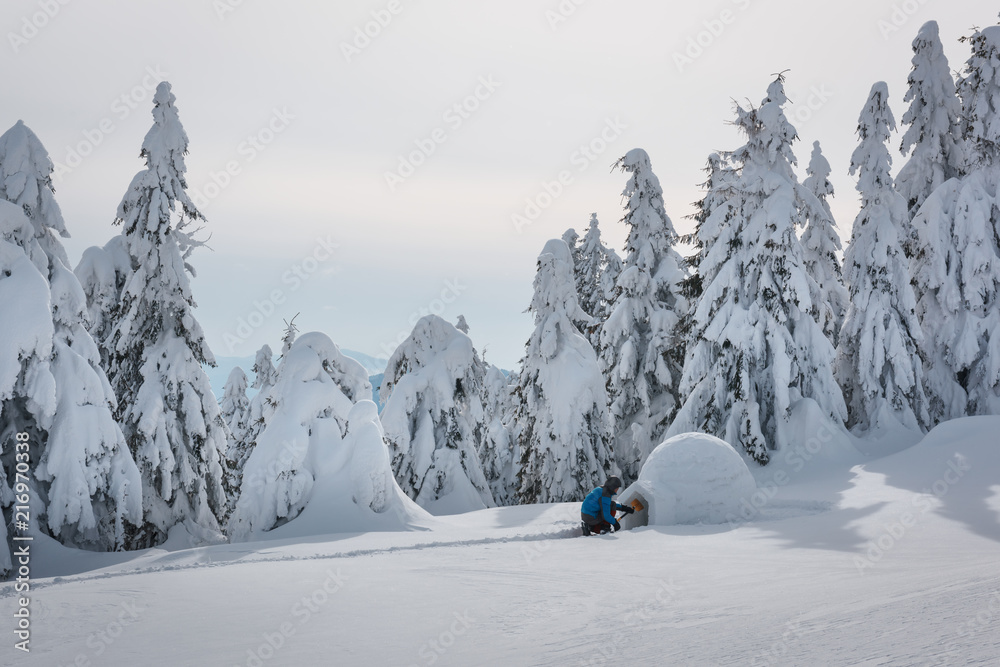 身穿蓝色夹克的男子在高山上建造冰屋。奇妙的冬季场景