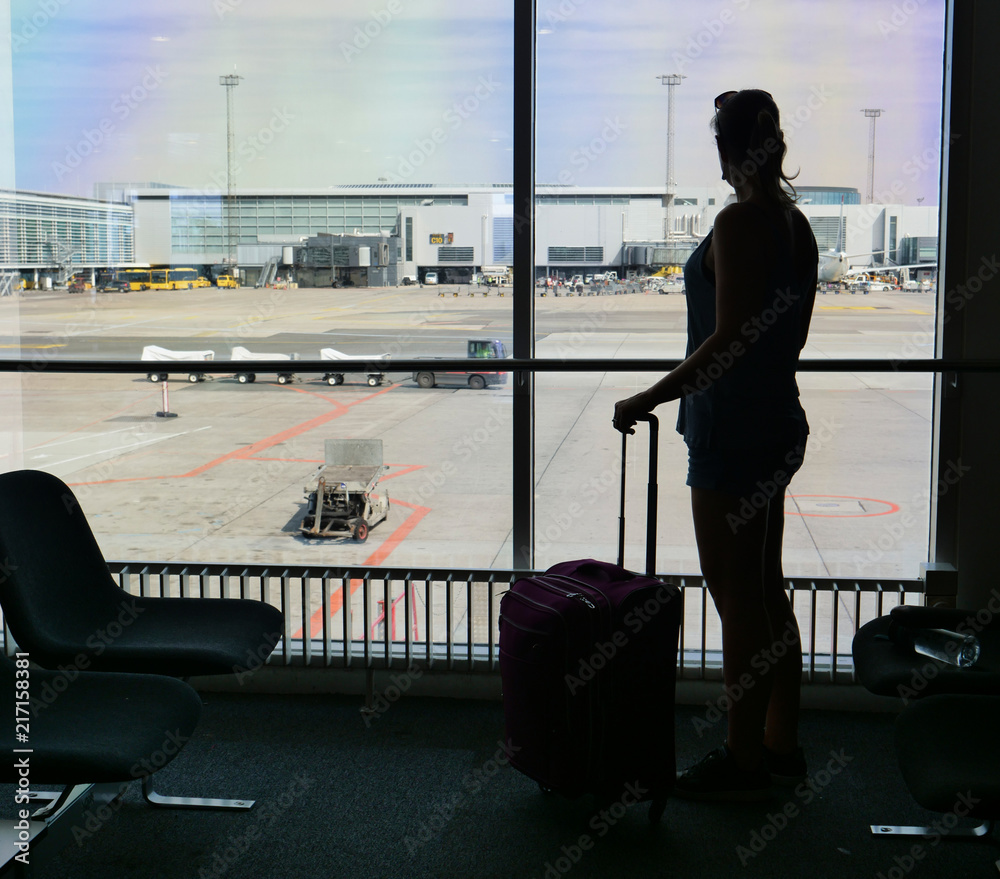 沉默：一名年轻女子站在窗户边，看着机场跑道。