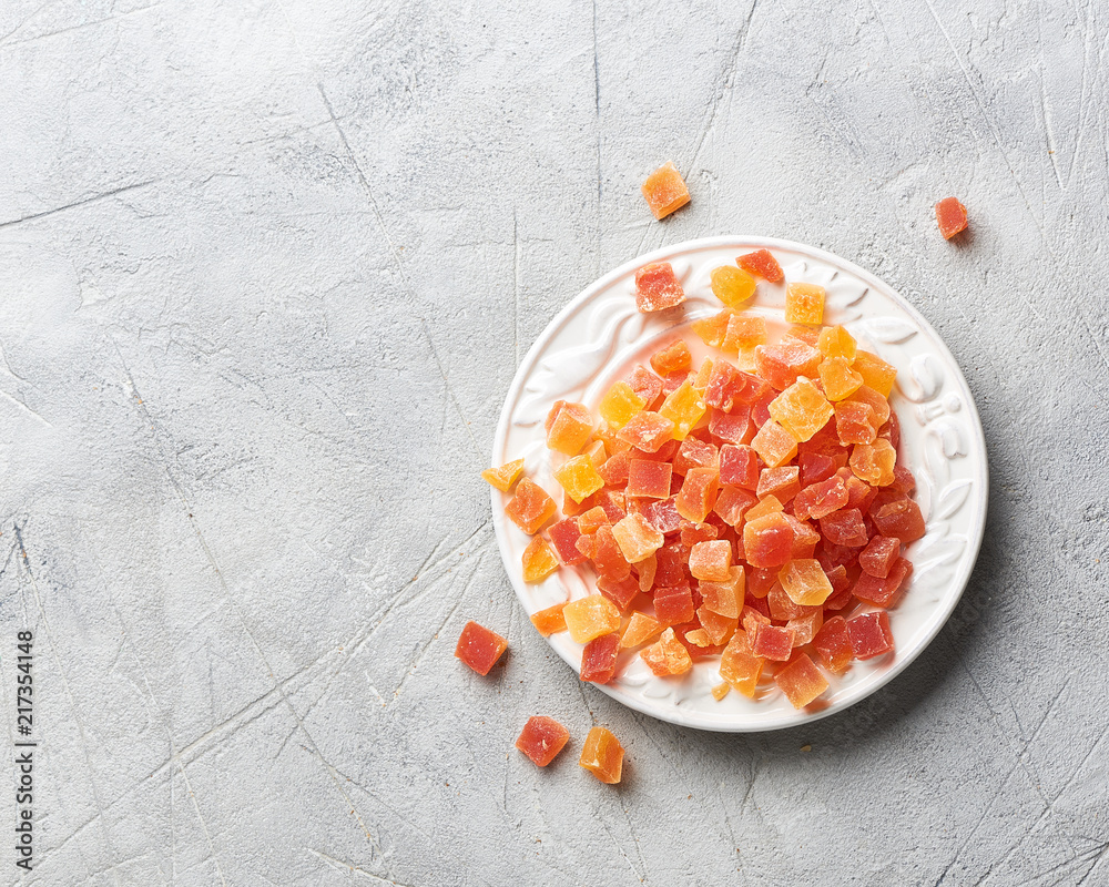 白色盘子里放着杏干、芒果和木瓜。灰色背景上的糖果，带co