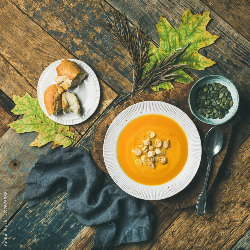 Flat-lay of fall warming pumpkin cream soup with croutons and seeds in plate on board over rustic wo