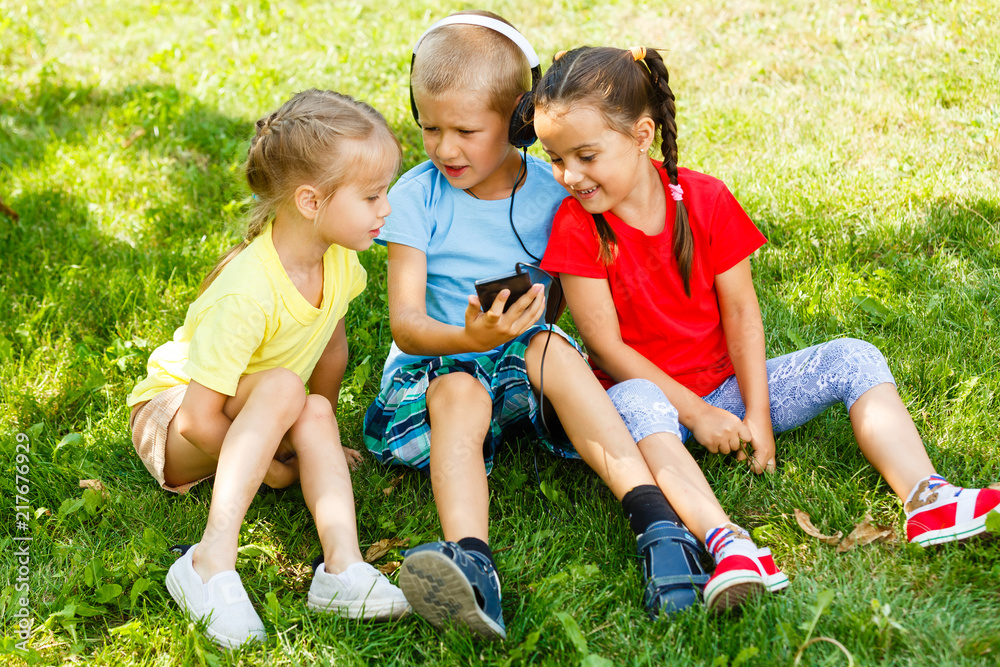 公园里三个孩子坐在草地上打电话