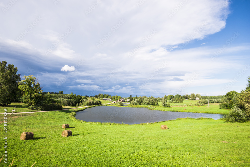 拉脱维亚小乡村湖的景色，背景是村庄和绿色森林