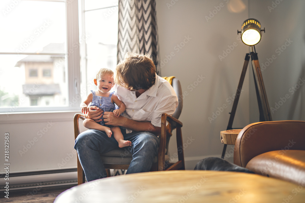 Young father with baby daughter on chair at home
