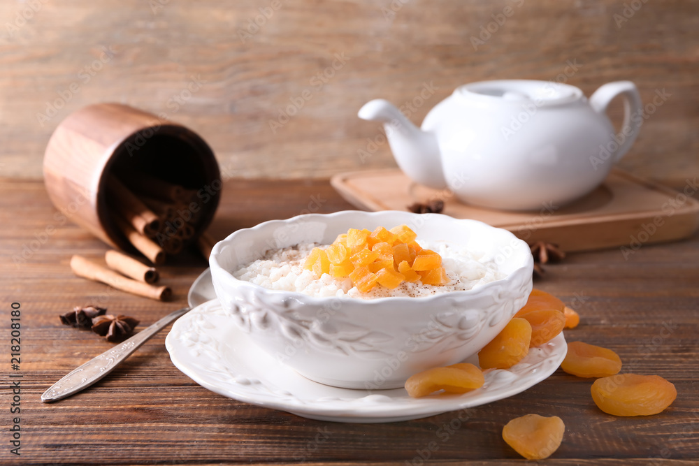 Bowl with delicious rice pudding and dried apricot on wooden table