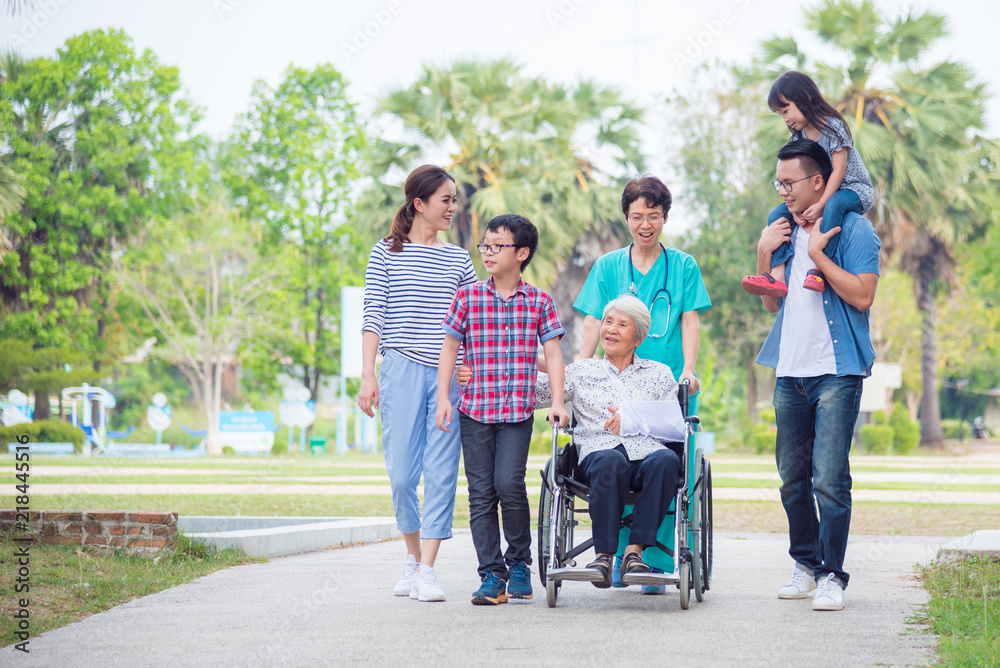 老年女性患者与家人和护士在医院公园里坐在轮椅上。