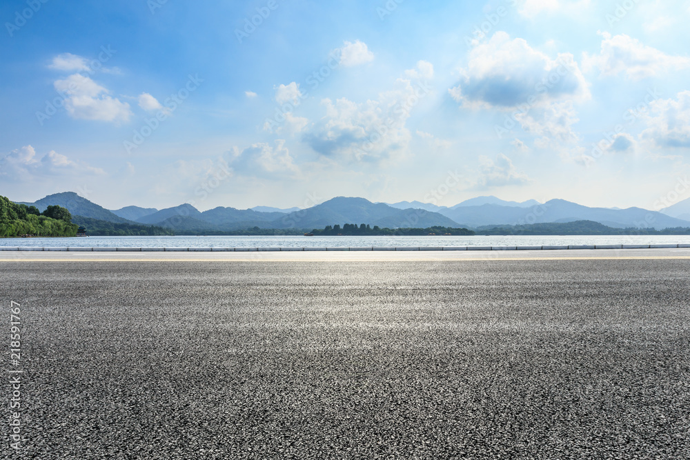 Empty asphalt road and lake with mountains on a sunny day