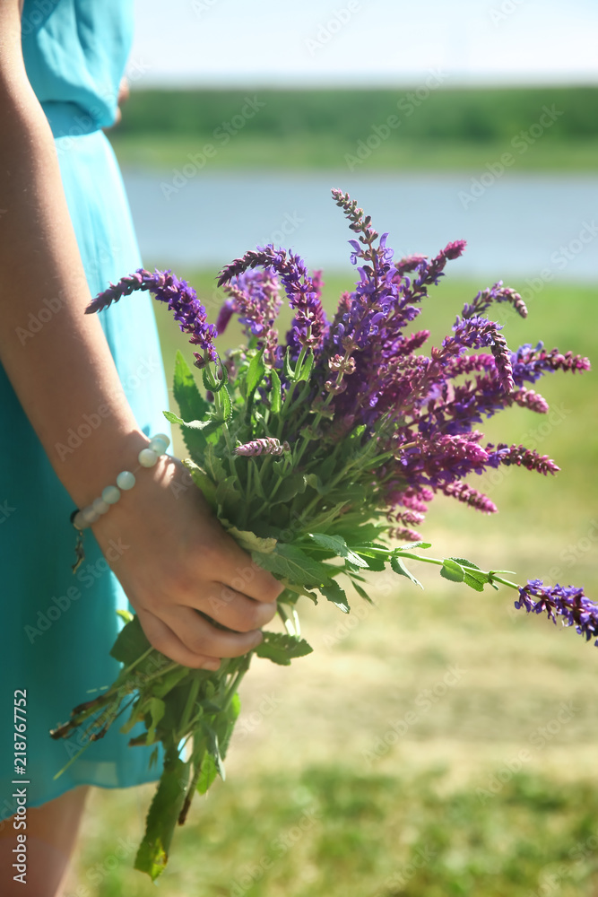 年轻女子在户外手持美丽的草地花朵，特写