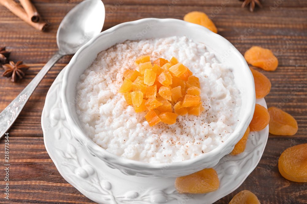 Bowl with delicious rice pudding and dried apricot on wooden table