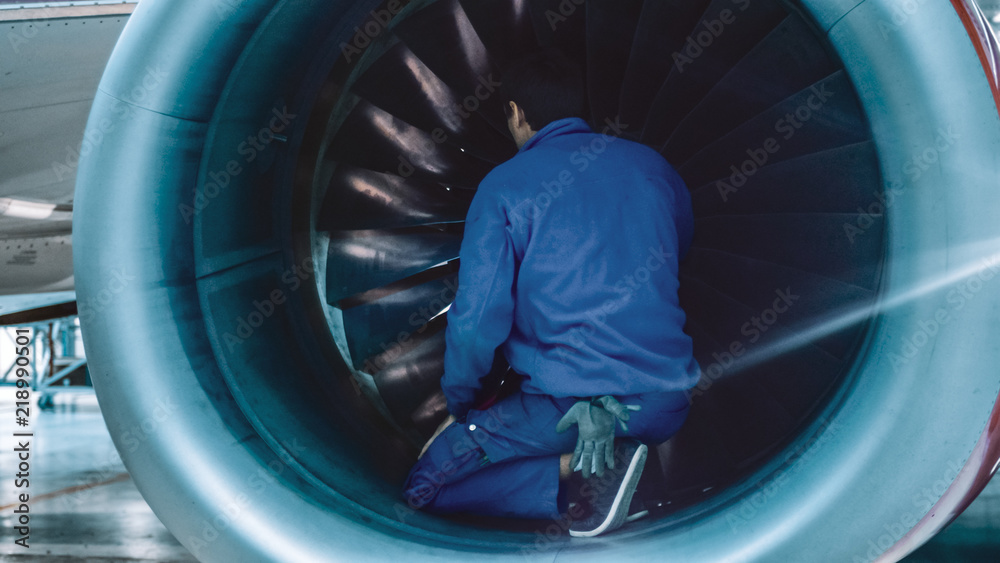 Aircraft maintenance mechanic with a flash light inspects plane turbine blades in a hangar.