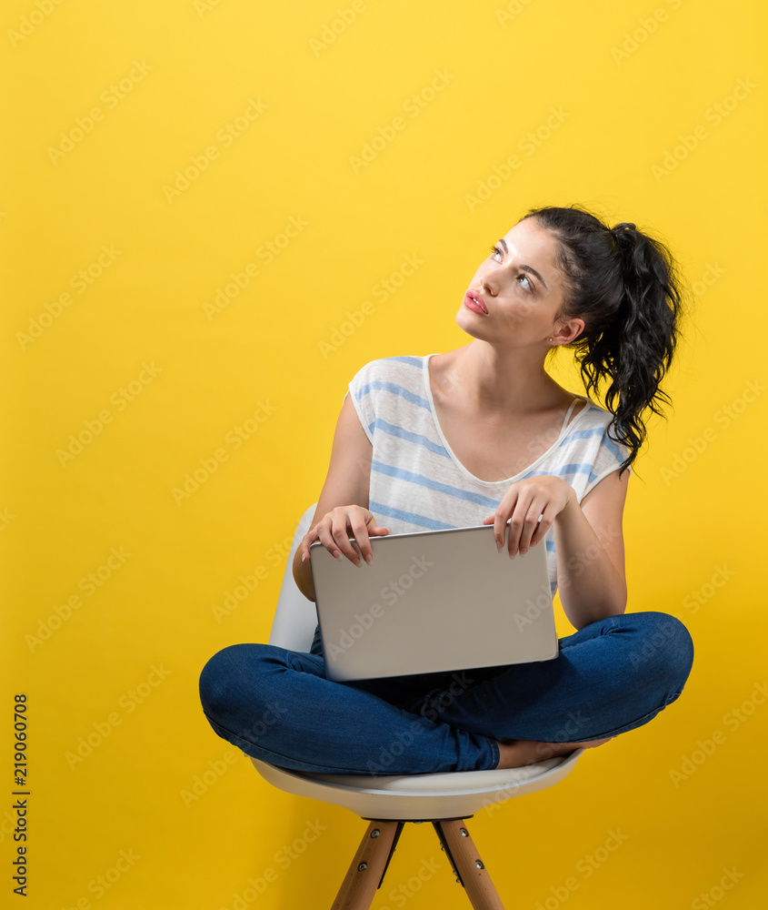 年轻女子在黄色背景下使用笔记本电脑