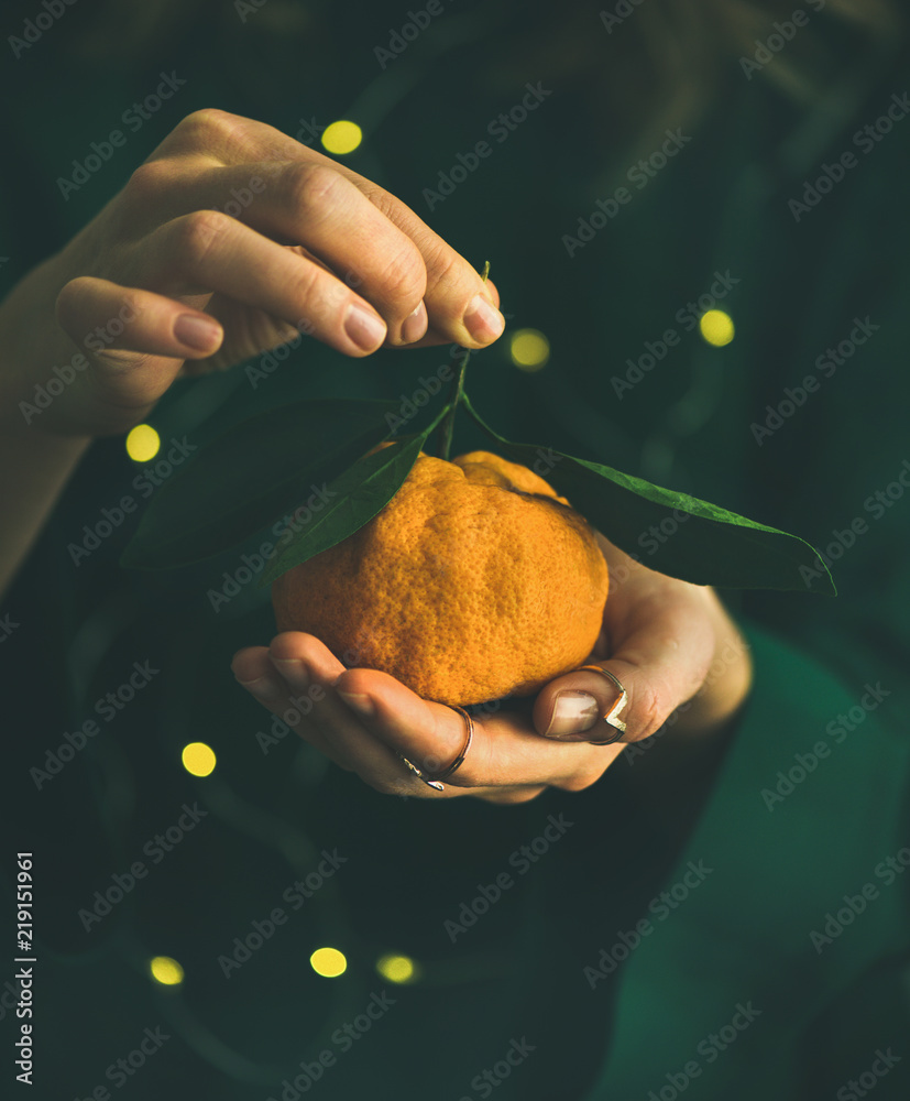 节日灯光下，身穿绿色连衣裙的女孩手中拿着新鲜的生柑橘果实和叶子