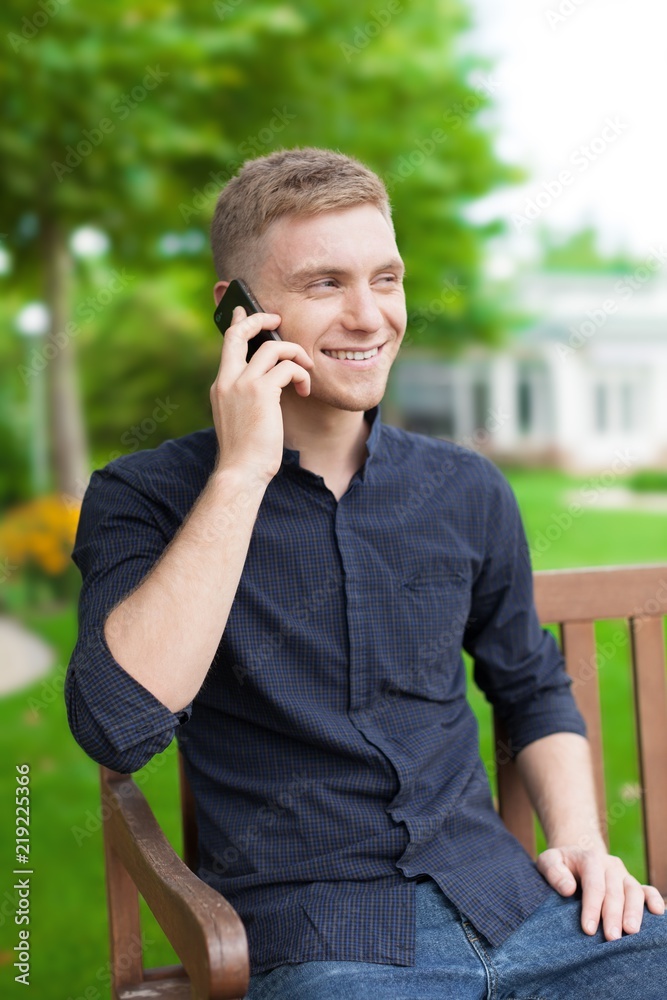 一个微笑的男人在公园长椅上打电话的肖像