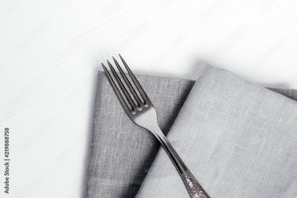 白色木桌上的钢叉和灰色布餐巾