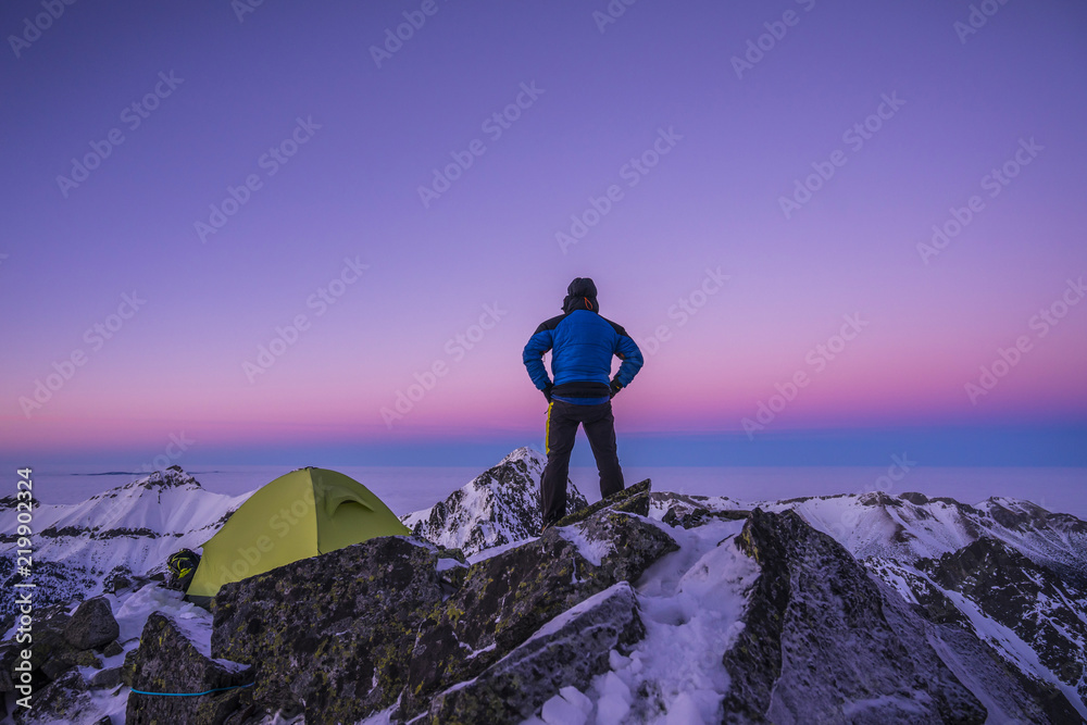 登山者站在山顶上的帐篷旁做饭。冬季登山探险