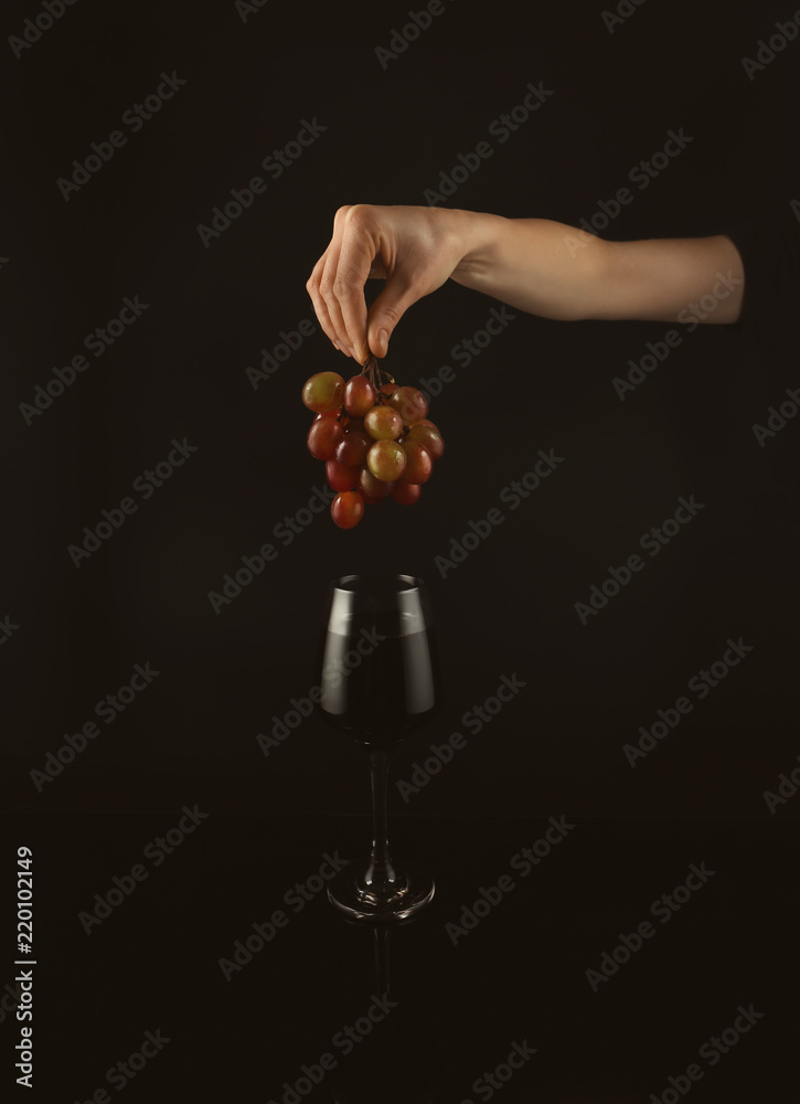 黑底红葡萄酒上的女手拿着葡萄