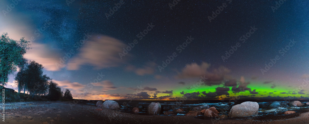 Beautiful panorama made on the beach with aurora borealis, milky way and starry sky.
