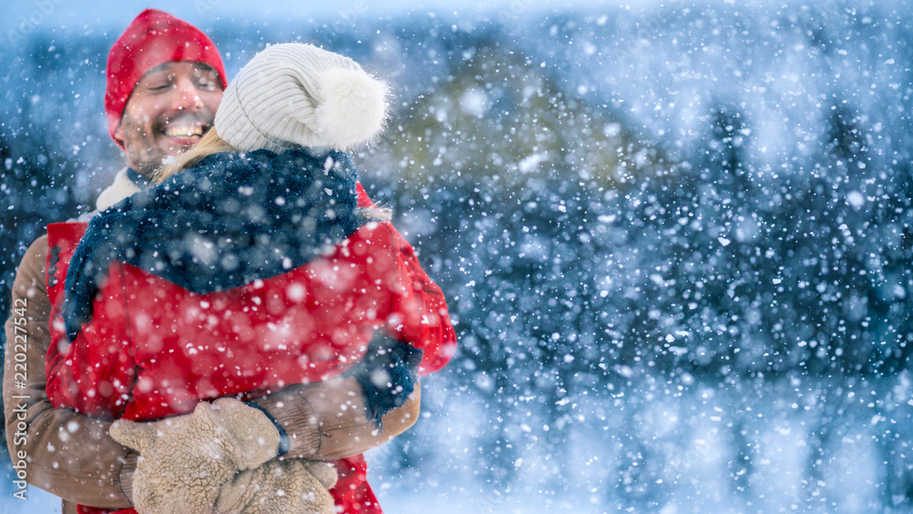 英俊的年轻情侣拥抱并幸福地微笑，雪落在他们身上。情侣在后院相爱