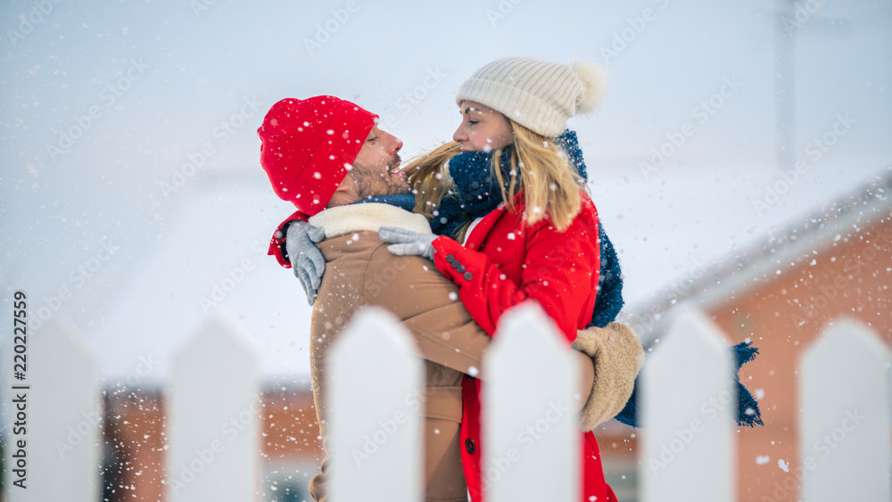 英俊的年轻夫妇拥抱并幸福地微笑，雪落在他们身上。后院里的情侣