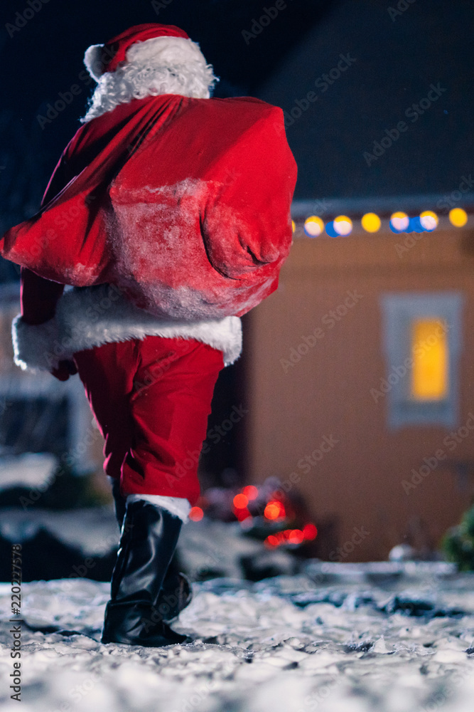 正宗圣诞老人把红袋子扔到肩上，走进Idylic Hous的前院