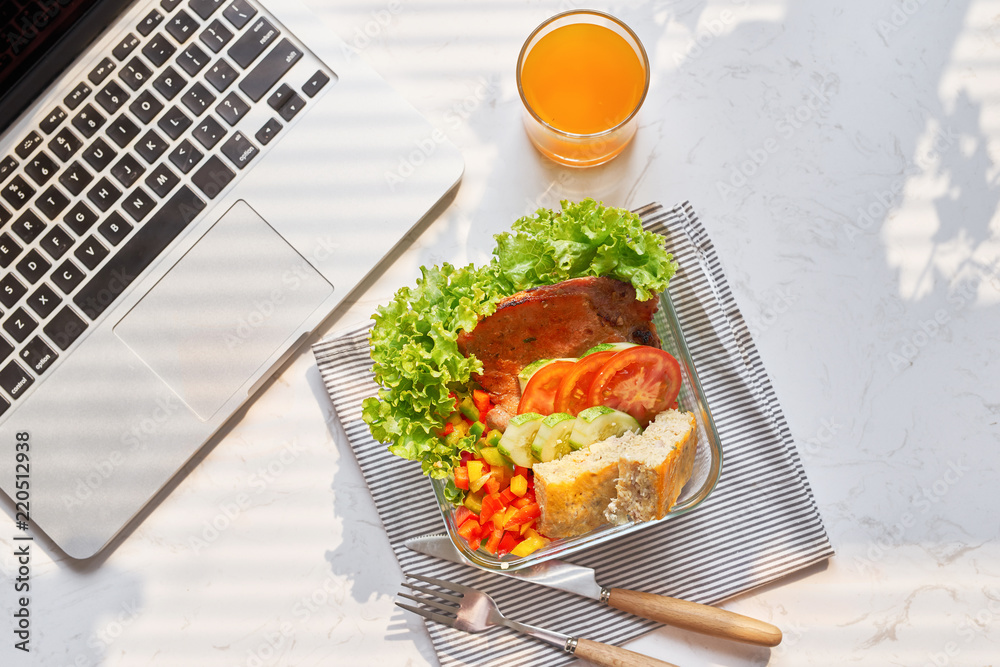 工作场所的笔记本电脑、玻璃杯中的橙汁和午餐盒中的新鲜沙拉俯视图