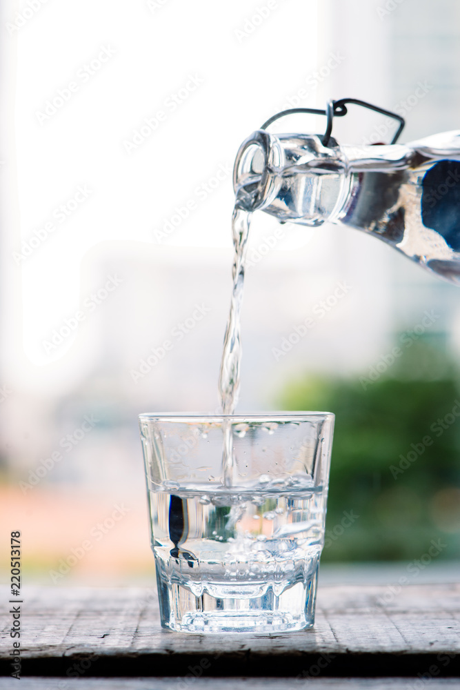 干净的饮用水从一个罐子里倒进一个放在木桌上的圆形玻璃杯和一个浅绿色的杯子里