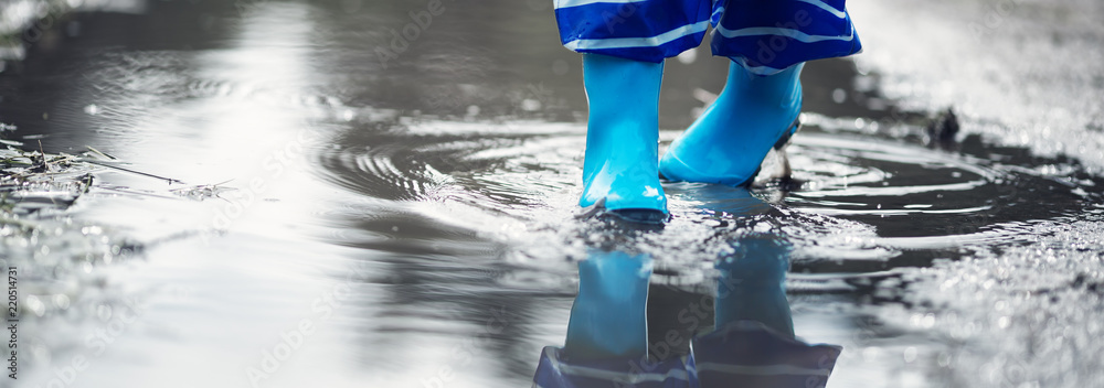 雨天孩子穿着雨鞋在水坑里行走。夏天男孩在雨中