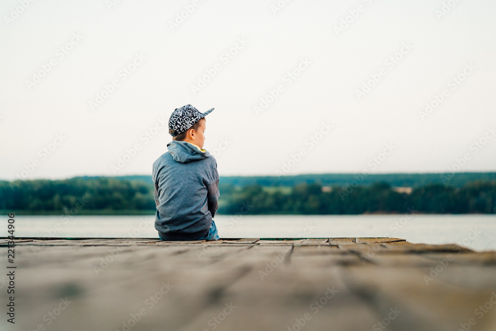 一个戴着时髦帽子和夹克的小男孩在湖边的桥上眺望远方。