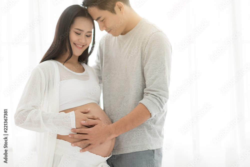 英俊的亚洲男子和他美丽的怀孕妻子站在w附近拥抱微笑