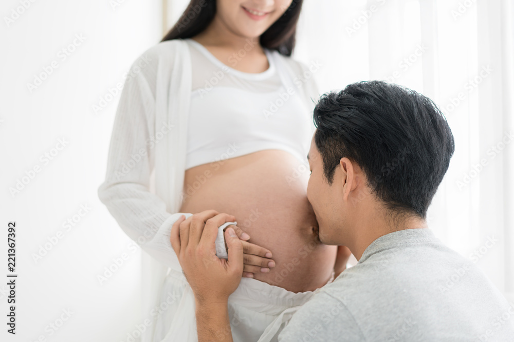 亚洲丈夫闭着眼睛亲吻妻子怀孕的肚子。亚洲已婚夫妇和家人