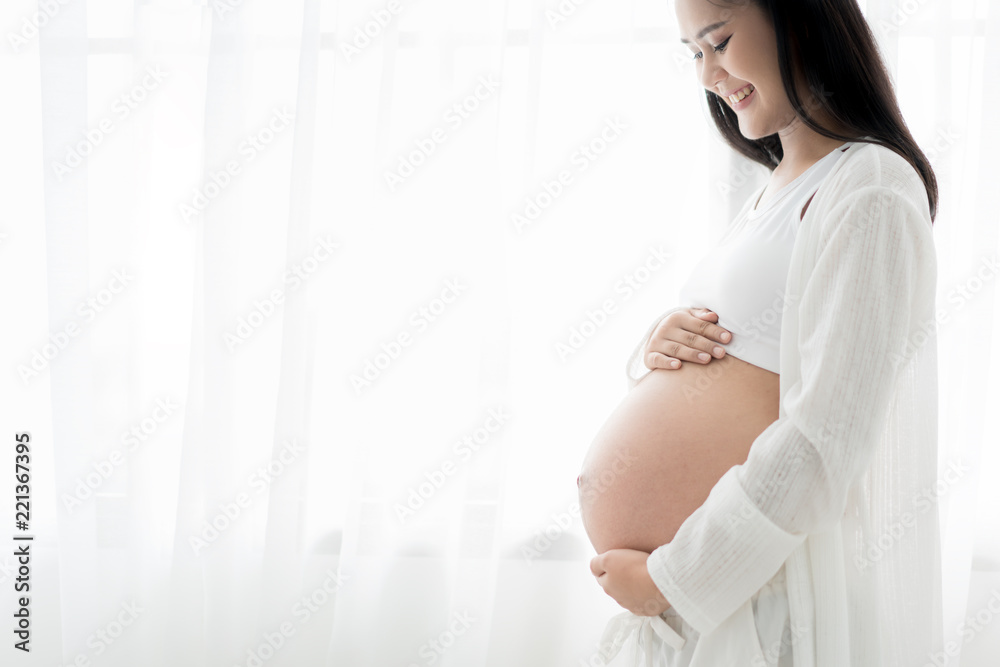 幸福微笑的孕妇在家里站着抚摸自己的肚子的特写。怀孕了，re