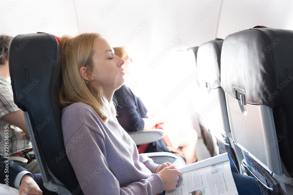 坐飞机旅行时，疲惫的金发白人女性在座位上打盹。商业交通