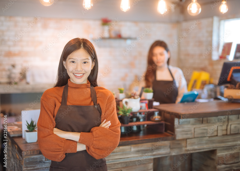 亚洲女服务员拿着菜单，穿着围裙，站在咖啡店里的肖像。