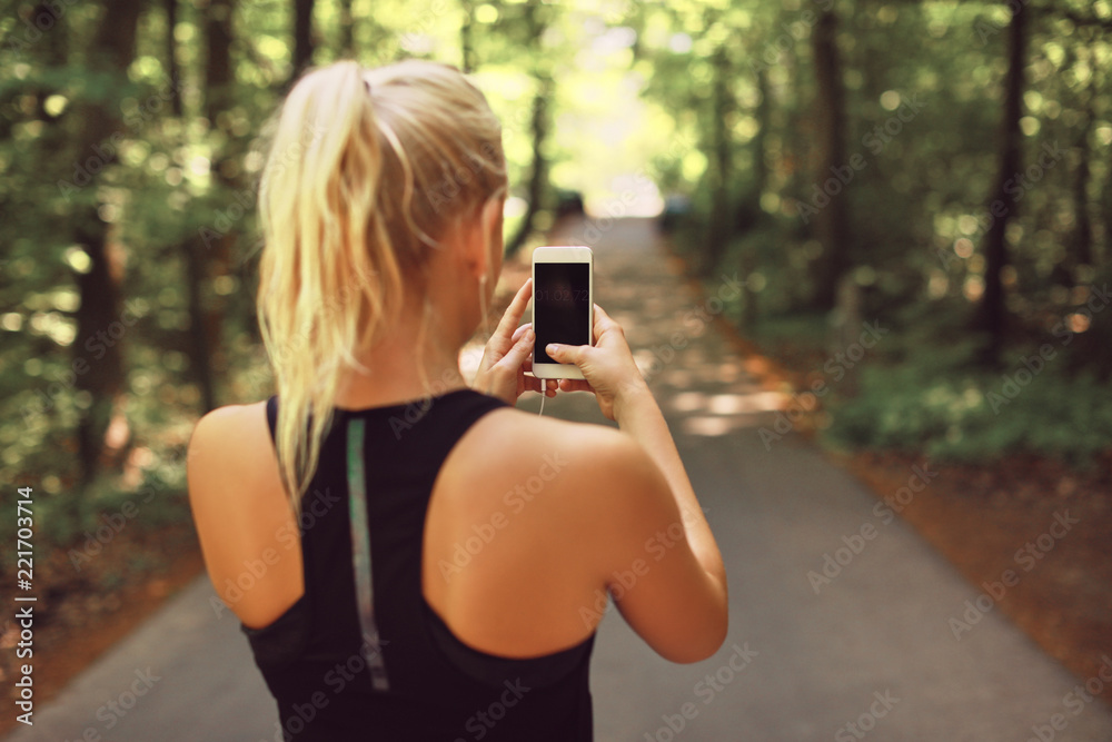 健康的女人在森林里跑步并使用手机