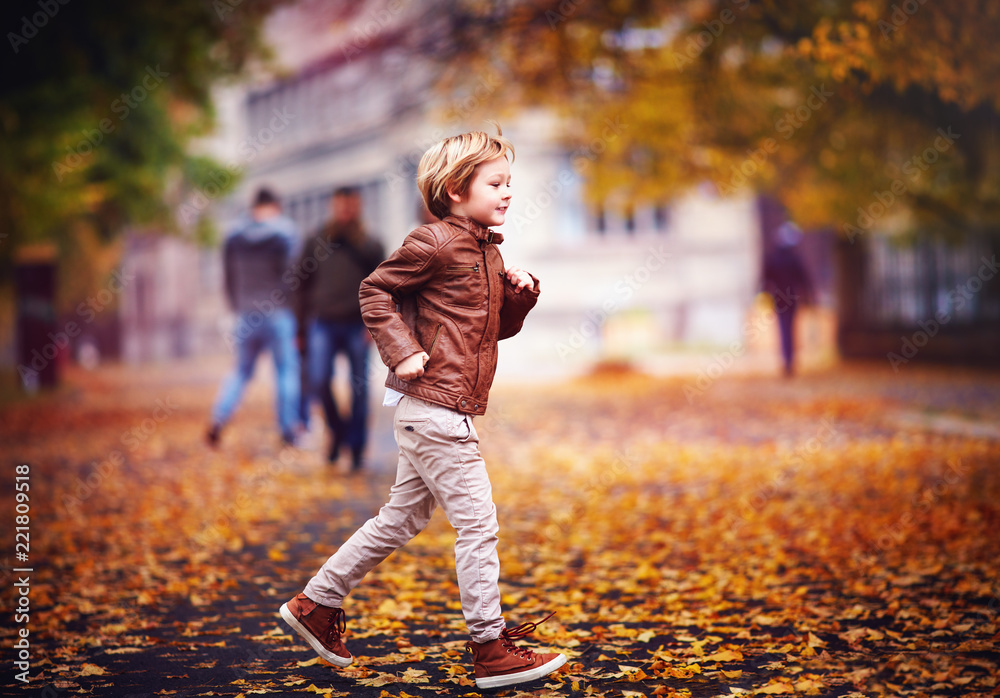 微笑的年轻男孩，在秋天的城市公园里，在落叶中玩耍的孩子
