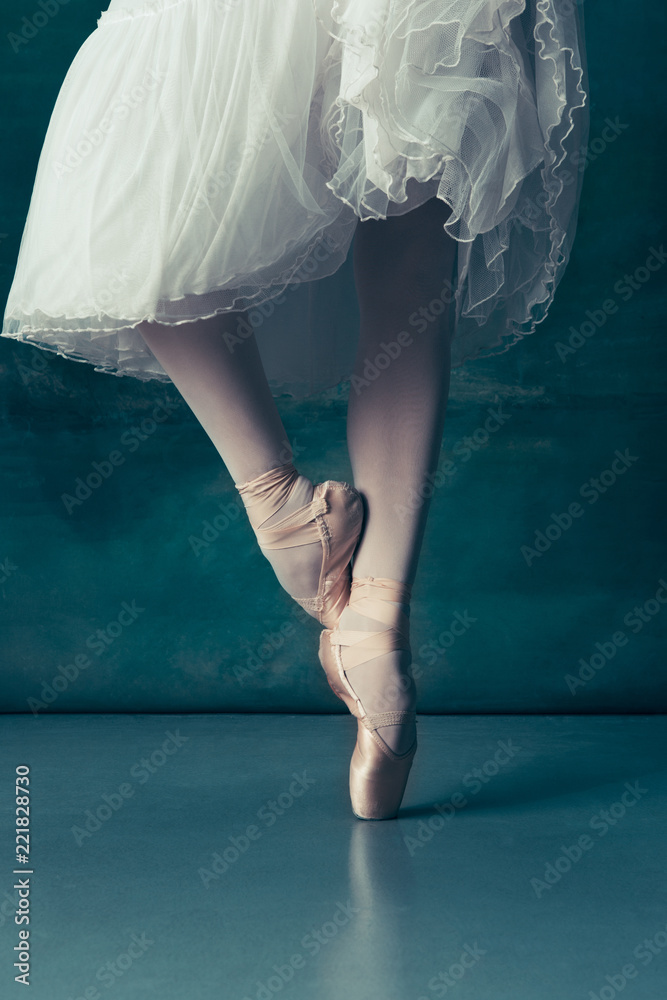 在灰色木地板上，用尖头鞋特写经典芭蕾舞演员的腿。芭蕾舞女与白人的项目