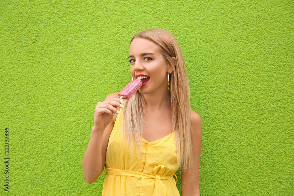 美丽的年轻女子在彩色墙附近拿着冰淇淋