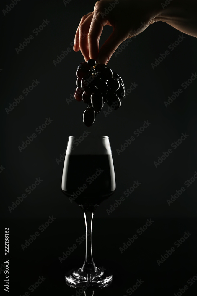 女性手拿葡萄在黑底红酒杯上