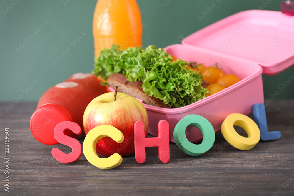木桌上用彩色字母做成的午餐盒，里面有美味的食物和单词SCHOOL