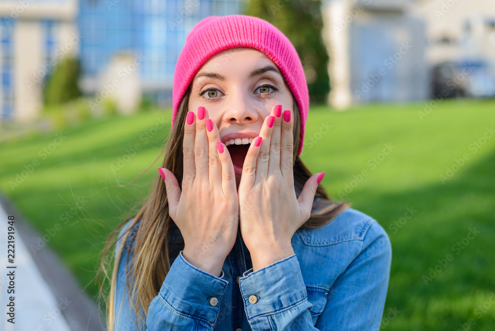 Happy joyful surprised  teenage girl in pink hat, with pink nails, dressed in jeans shirt covering h