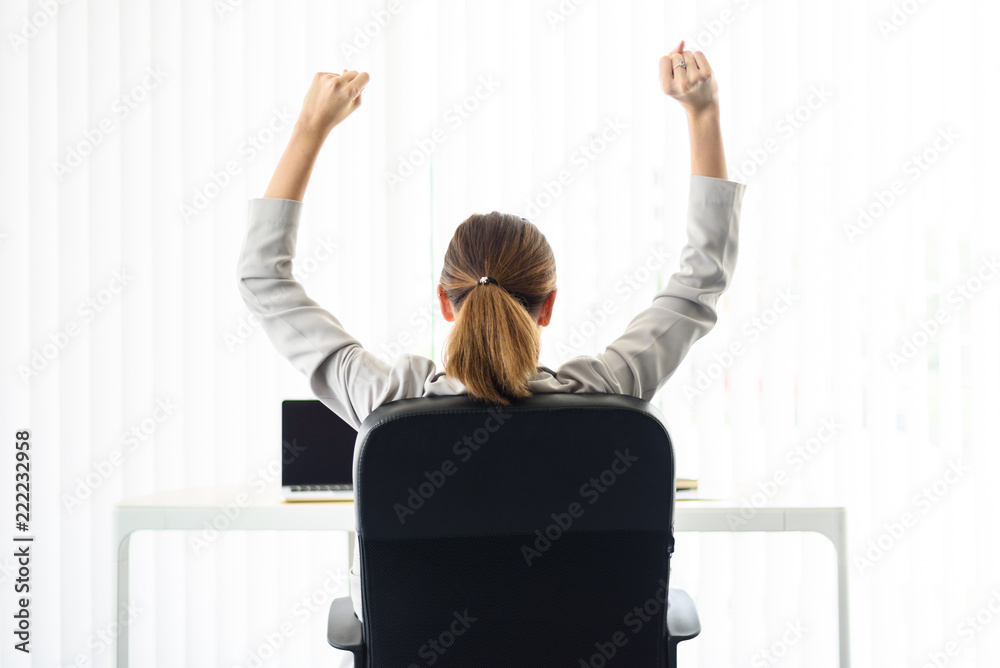 幸福满意的商业女性在空中伸展双臂，坐在黑色椅子上放松