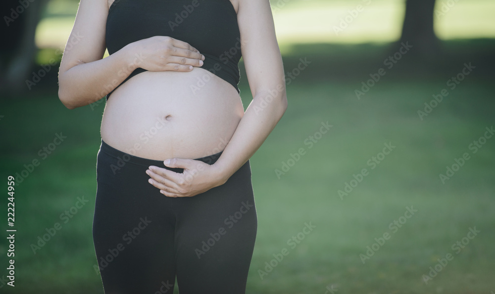 孕妇穿着黑色瑜伽服，在户外用手抱着肚子的短镜头。