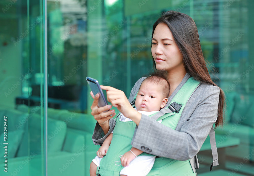 穿着西装的商业妈妈用智能手机抱着符合人体工程学的婴儿