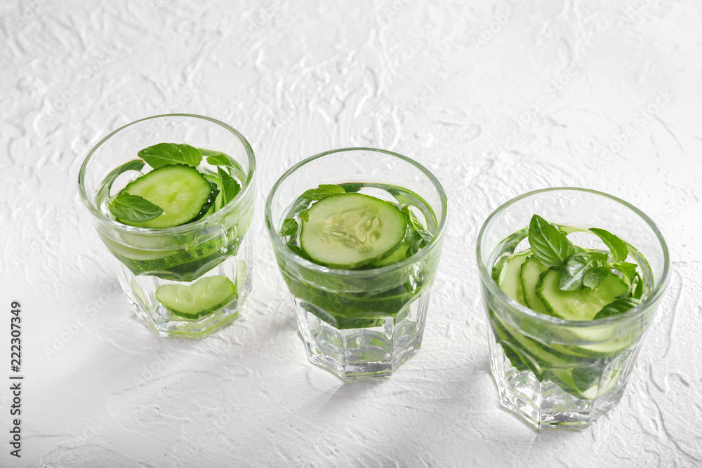 Glasses of cucumber infused water on white textured background