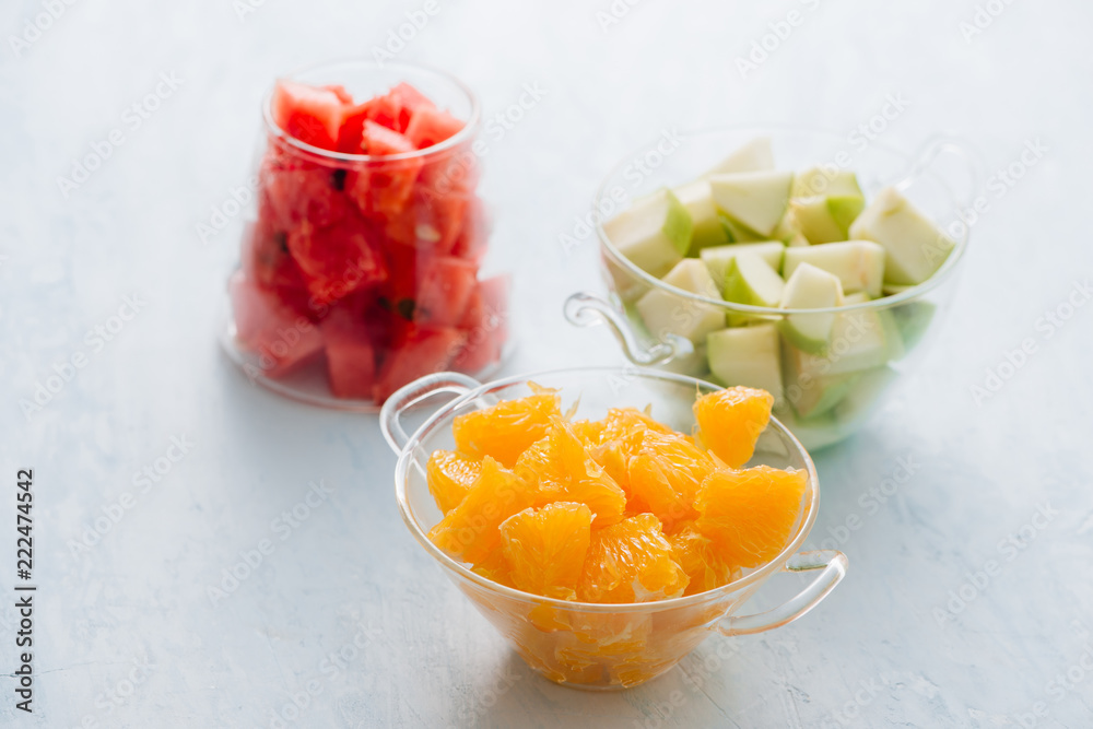 Pieces of tropical fruits in a glass. Sliced orange, apple, slices of watermelon in glass bowl. Citr
