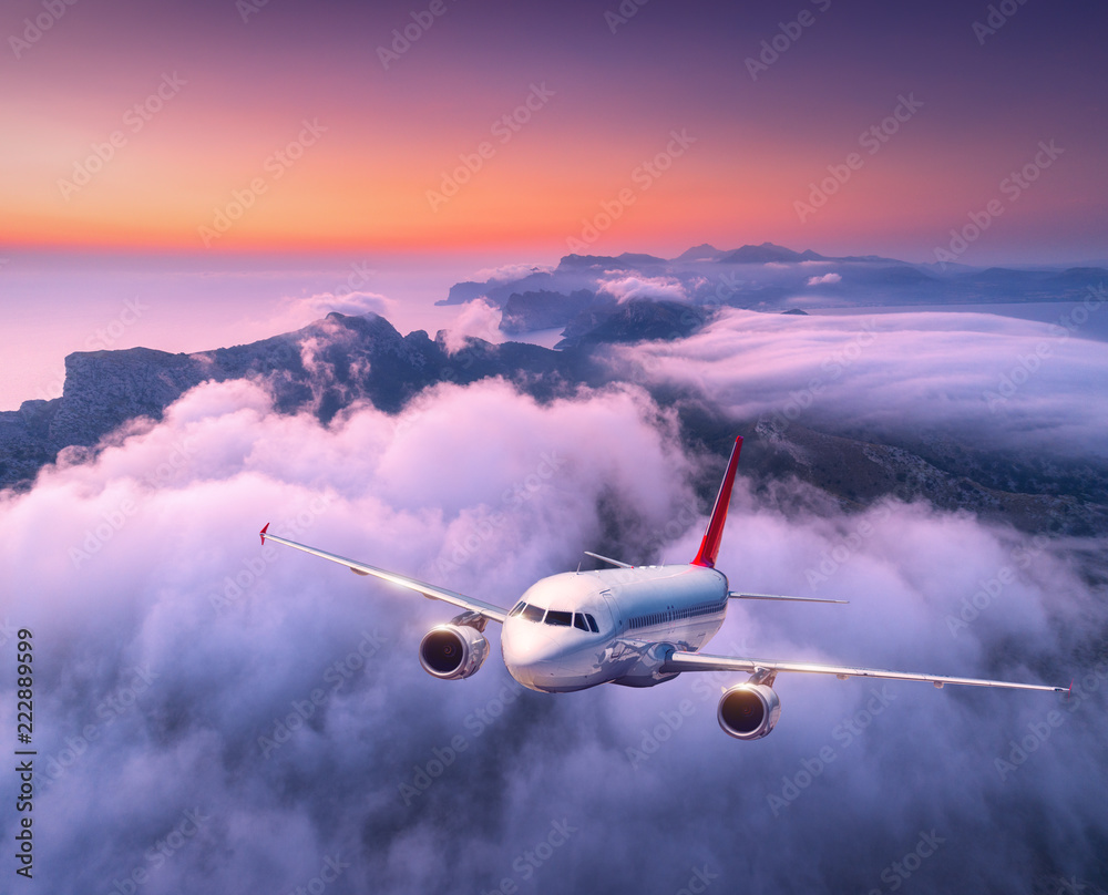日落时，客机在云层上飞行。白色大飞机、低云、大海的景观，