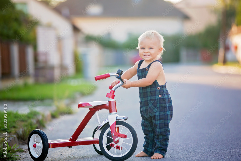 可爱的蹒跚学步的孩子，男孩，在街上玩三轮车，孩子在日落时骑自行车